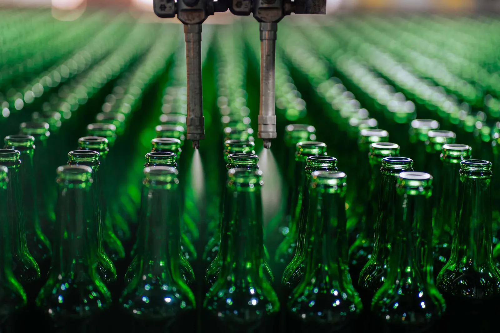 Rows of green glass bottles on an automated production line in a factory setting. Stock photo illustrating Patil Automation's fund raise story.