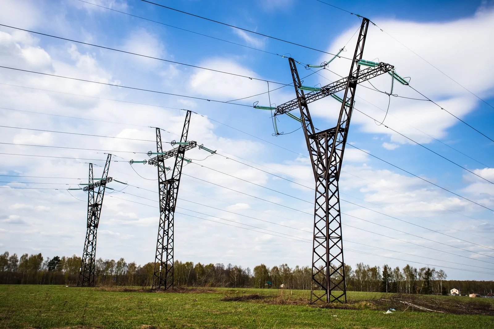 High voltage electric towers stand tall over a clear sky and grassy field, providing a serene landscape view. Stock photo illustrating Transrail Lighting's earning call story.