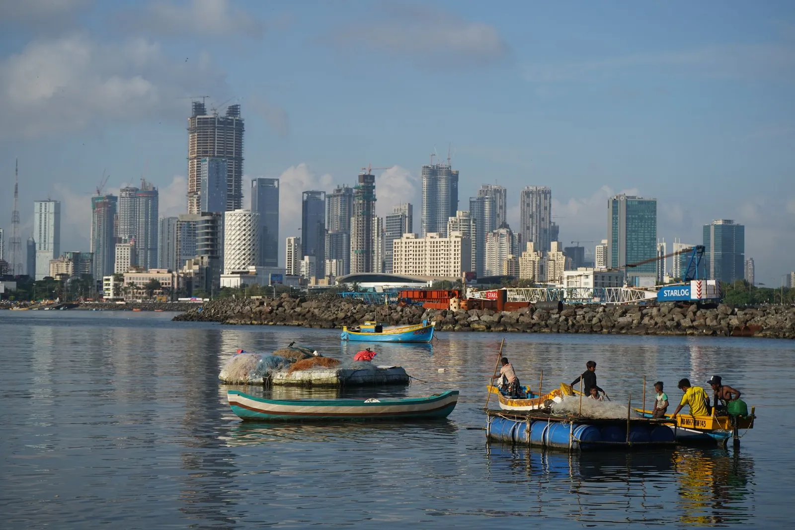 Vibrant view of Mumbai's skyline with local fishing boats on the water, capturing urban and traditional life. Stock photo illustrating Man Infraconstruction's partnership story.