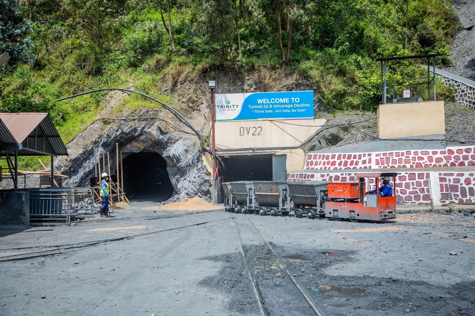Mining entrance with tunnel BV22, rail cars, and workers in safety gear at Trinity site. Stock photo illustrating JK Cement's expansion story.