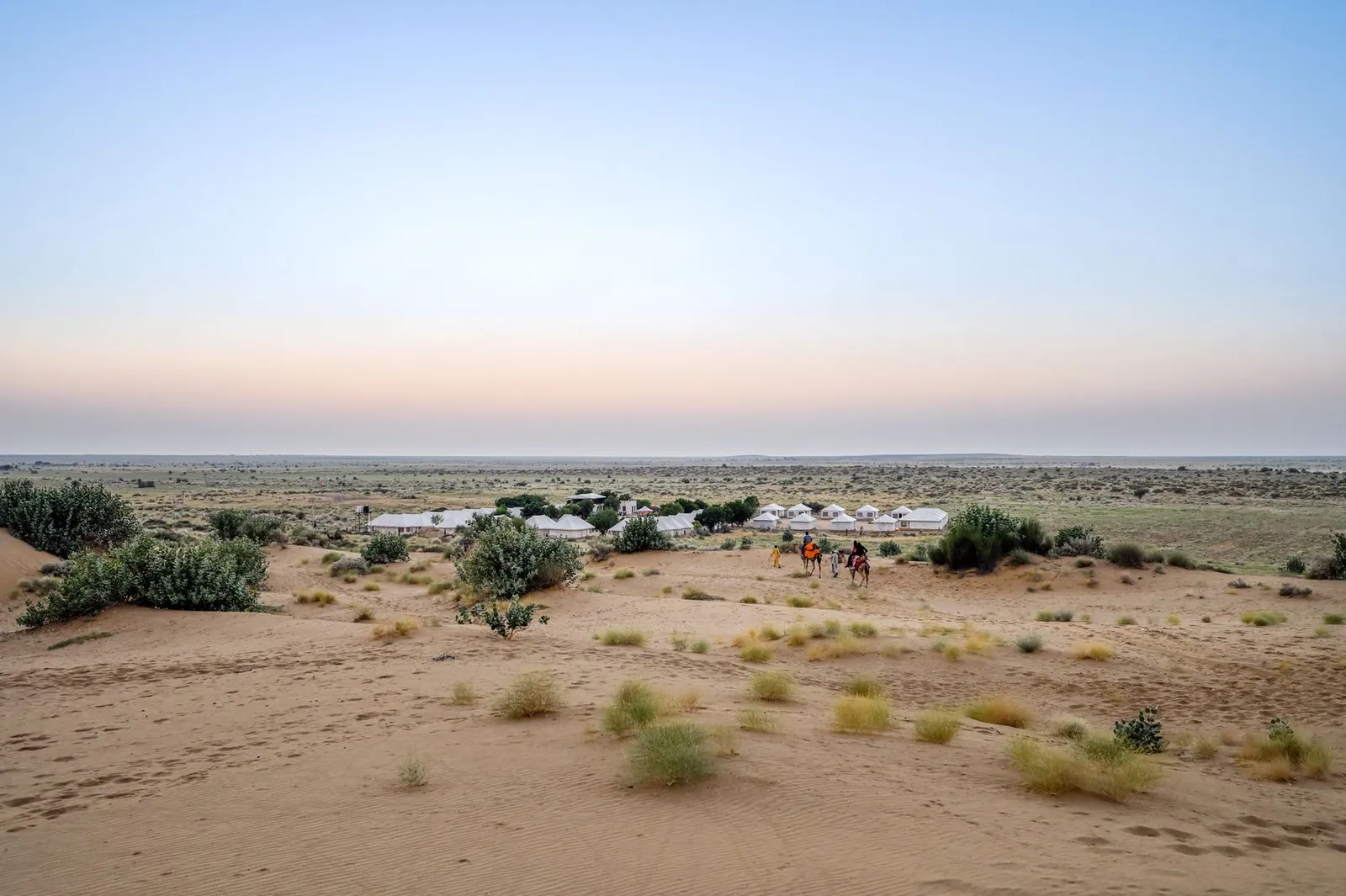 Desert sunset over a camel caravan and tents in Jaisalmer, India, showcasing serene arid landscapes. Stock photo illustrating Clean Max Enviro Energy Solutions' production started story.