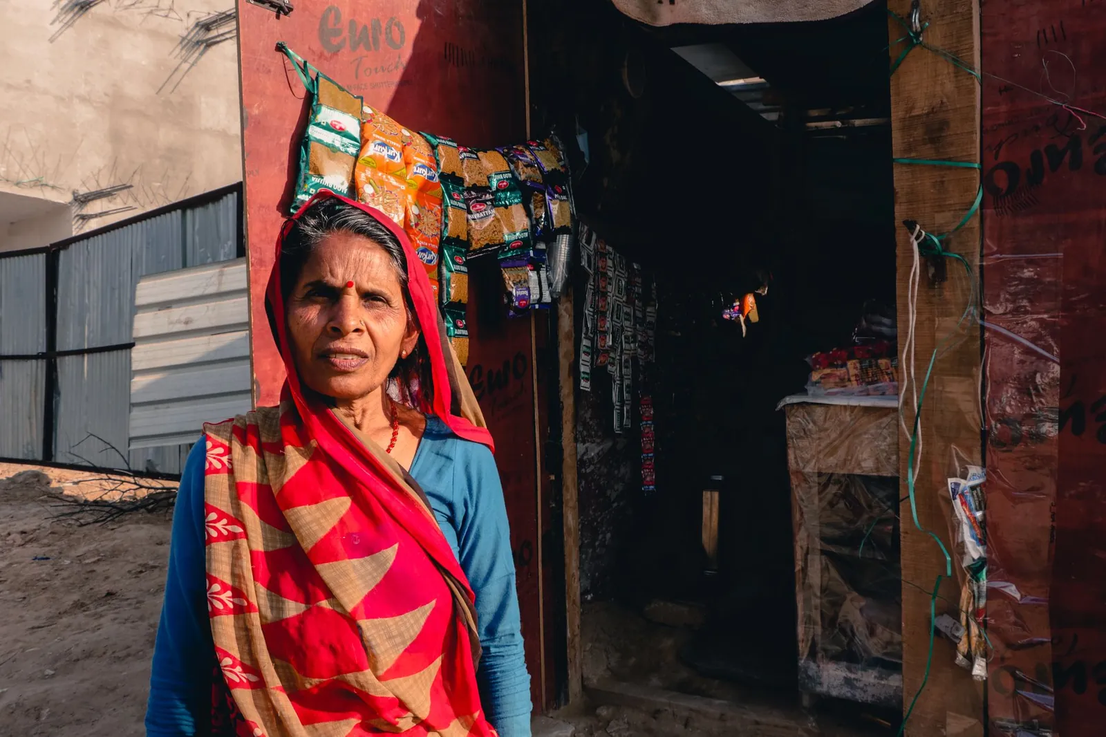 Portrait of an elderly Indian woman in traditional sari standing outside a small local shop. Stock photo illustrating Muthoot Microfin's earning call story.