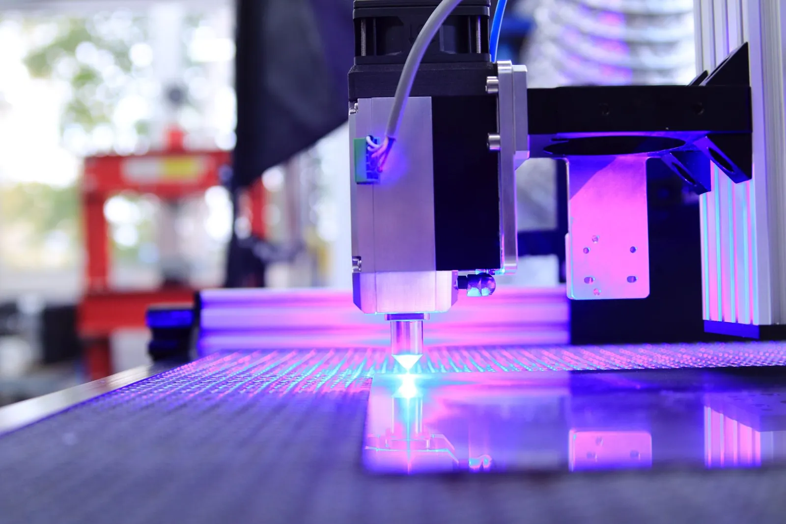 Close-up of a laser engraving machine working indoors with blue light reflection. Stock photo illustrating Kabra Extrusiontechnik's fund raise story.