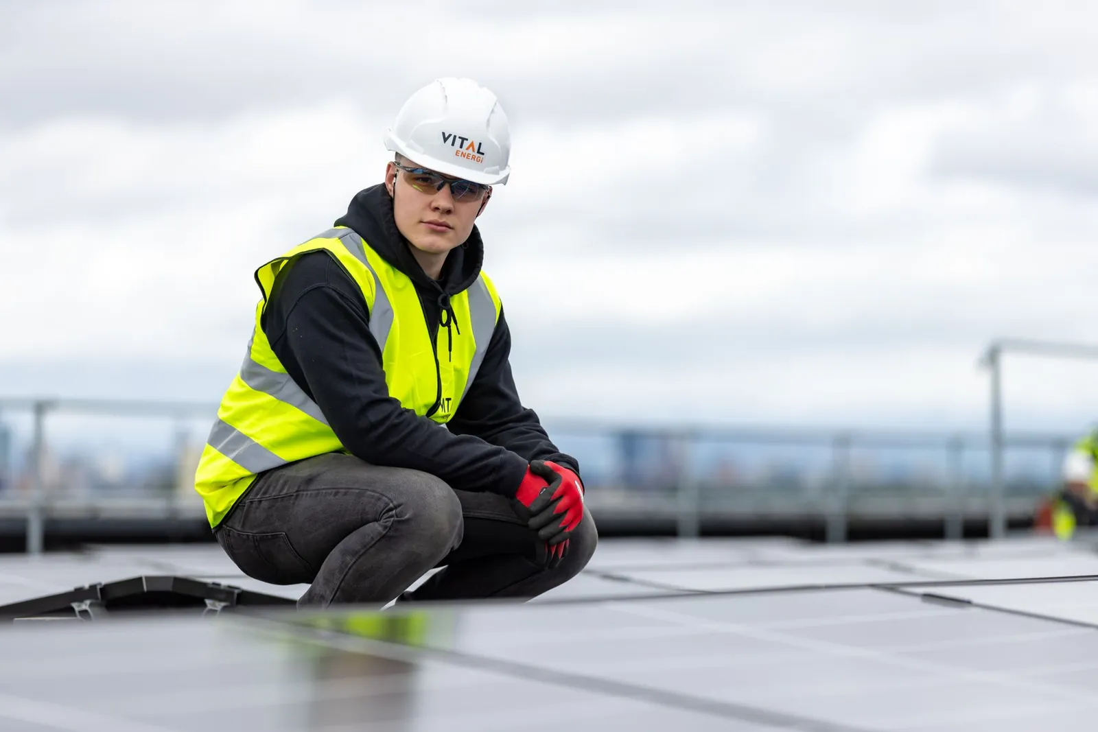 A construction worker inspects rooftop solar panels, wearing safety gear and high visibility vest. Stock photo illustrating Bondada Engineering's new order story.
