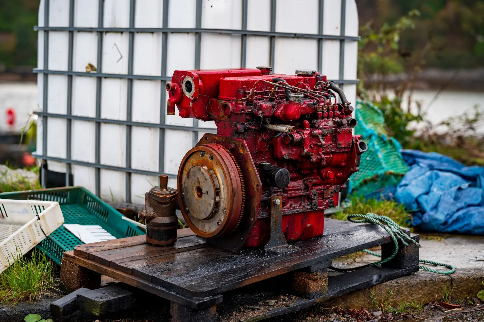 A rustic red diesel engine on a wooden pallet outdoors, surrounded by industrial objects. Stock photo illustrating Cummins India's product launched story.