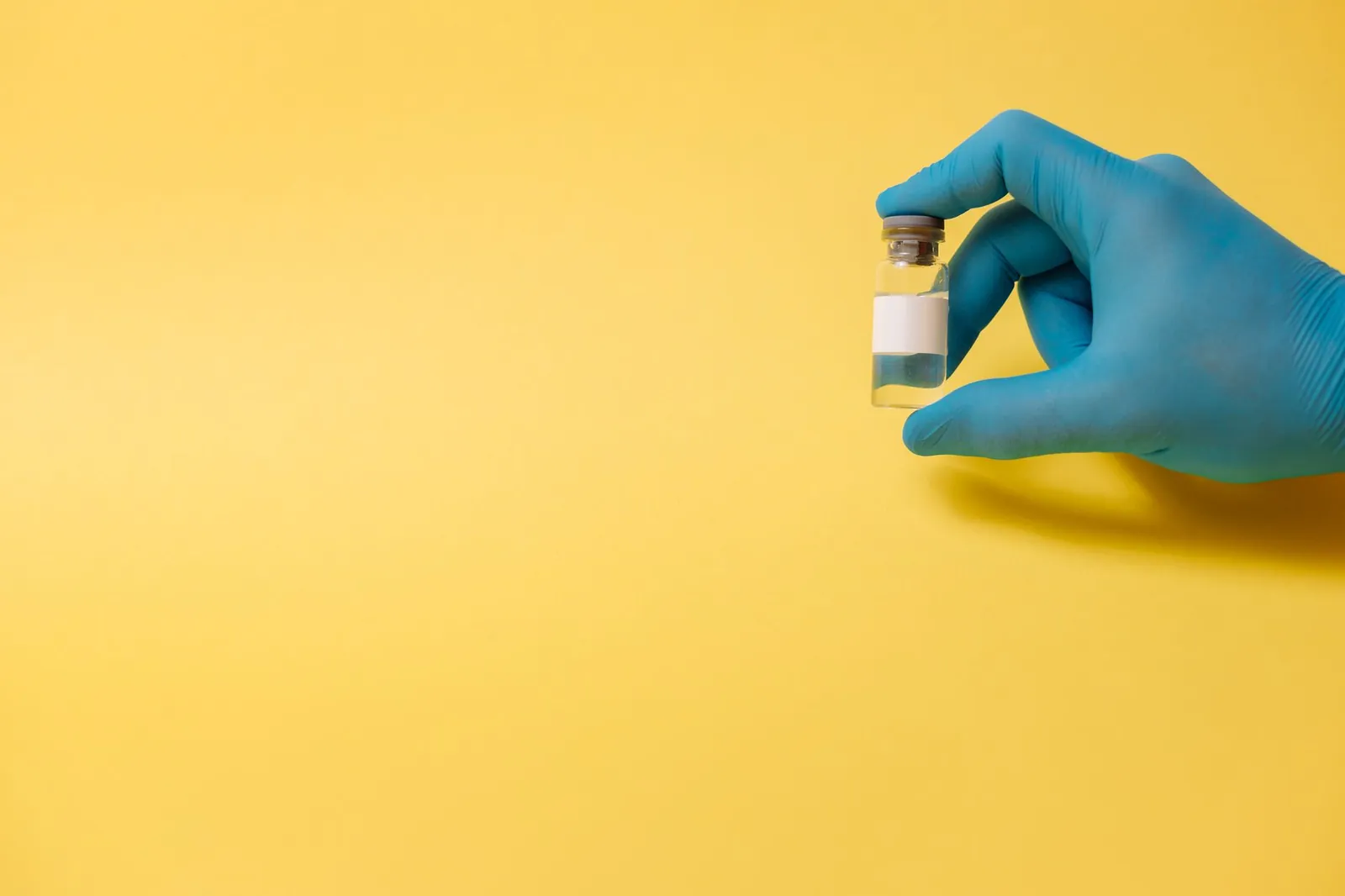 A gloved hand holds a medical vial against a bright yellow background, symbolizing health and medicine. Stock photo illustrating Gland Pharma's product launched story.