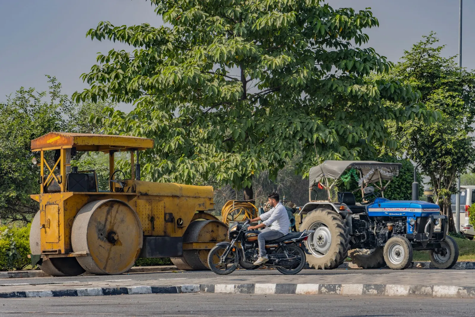 Traffic scene in Deeg, Uttar Pradesh with bike, roller, and tractor on a rural road. Stock photo illustrating PNC Infratech's new order story.