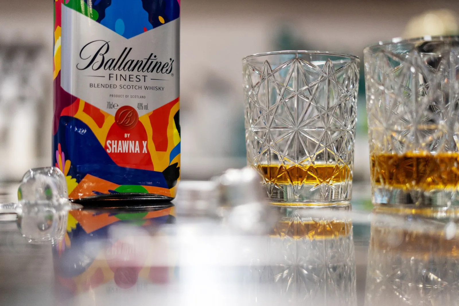 A vibrant Ballantine's whisky bottle and glasses on a reflective surface with ice cubes. Stock photo illustrating Allied Blenders and Distillers' product launched story.