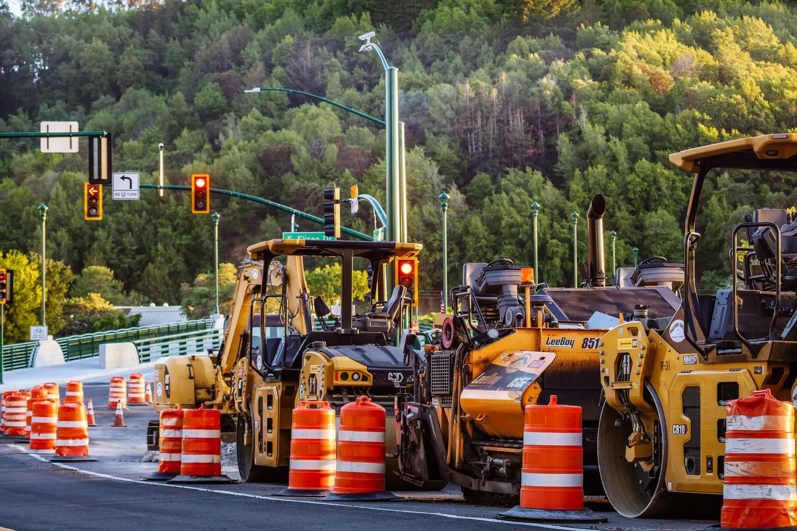 Heavy machinery and barriers at a road construction site with traffic lights and forest backdrop. Stock photo illustrating Dilip Buildcon's earning call story.