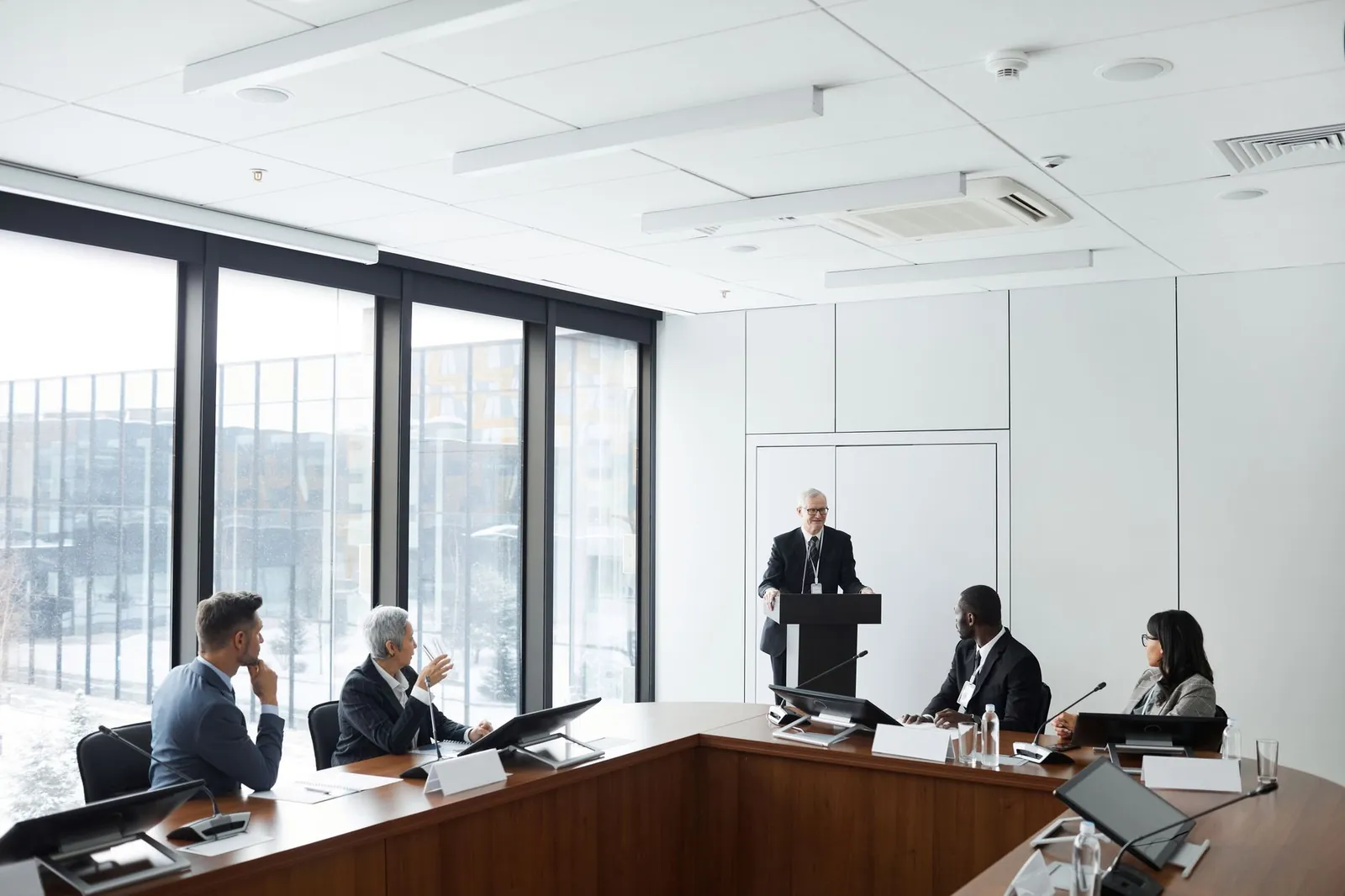 Corporate meeting with diverse professionals listening to a speaker at a podium in a modern conference room. Stock photo for the ALFA News guide: How to Read Corporate Announcements: A Practical SEBI Guide.