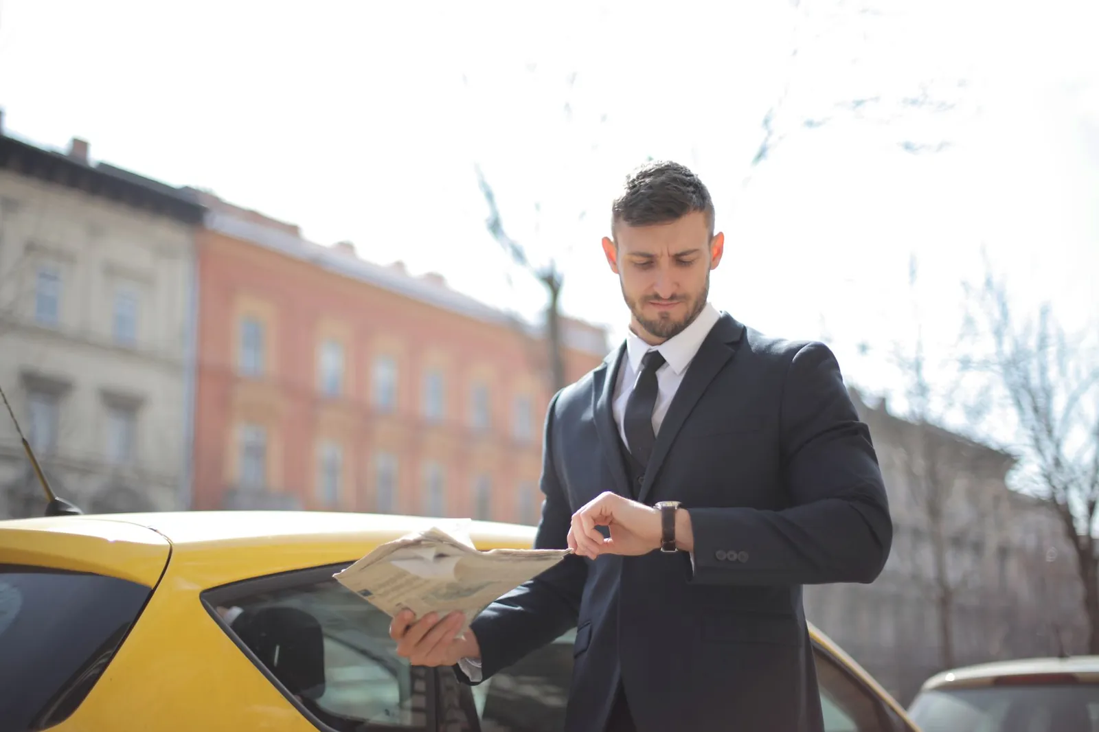 Corporate professional holding newspaper checks watch near a yellow car outdoors. Stock photo for the ALFA News guide: How to Track Corporate Announcements Daily in Indian Markets.