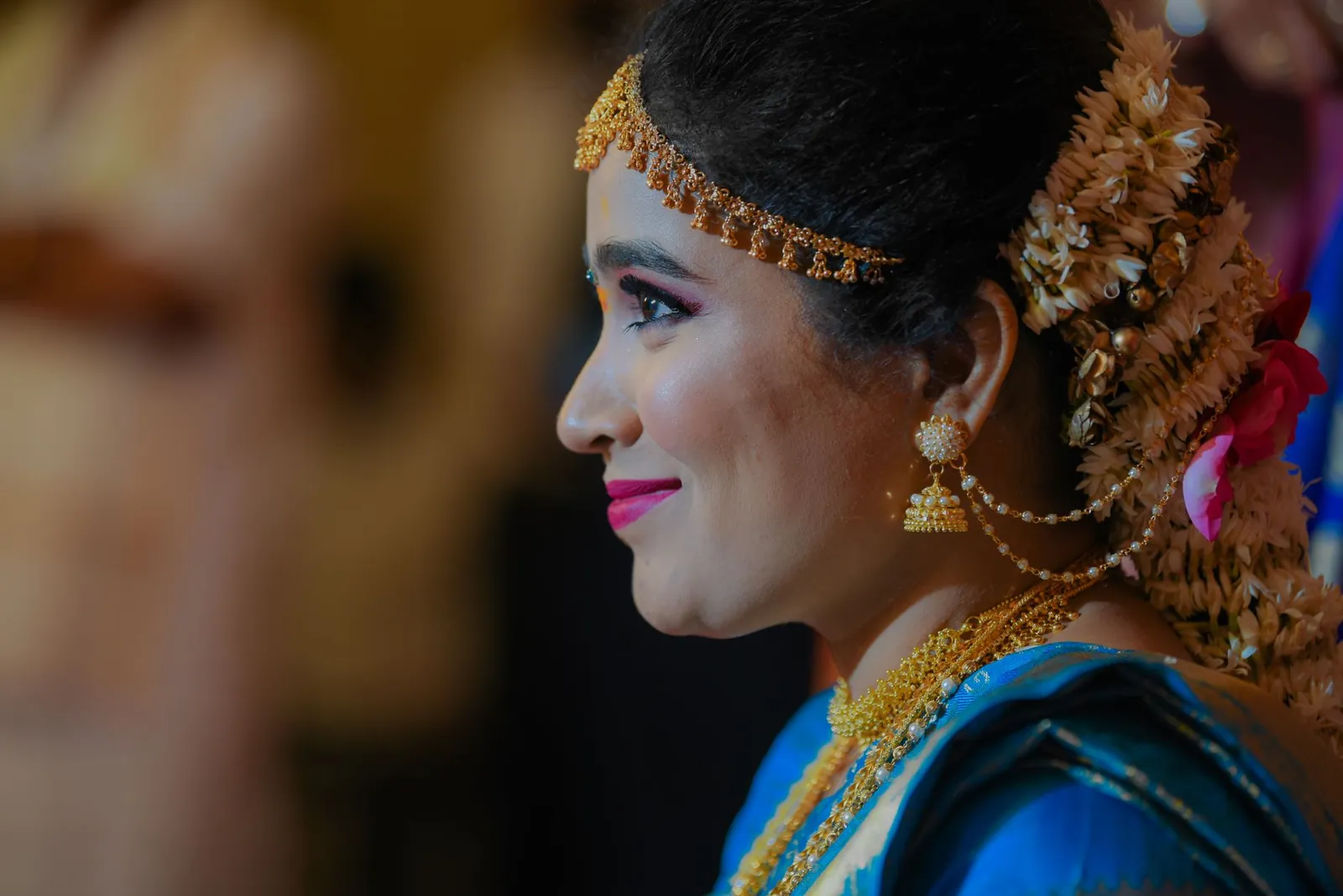Close-up profile of an Indian woman dressed in traditional attire with gold jewelry and flowers in her hair, smiling gracefully. Stock photo illustrating Shanti Gold International's earning call story.