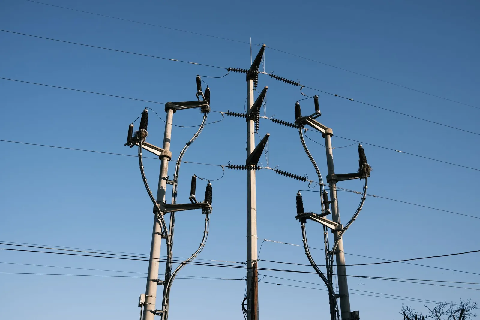 High-voltage power lines and poles silhouetted against a clear blue sky, representing energy distribution. Stock photo illustrating Marine Electricals (India)'s new order story.
