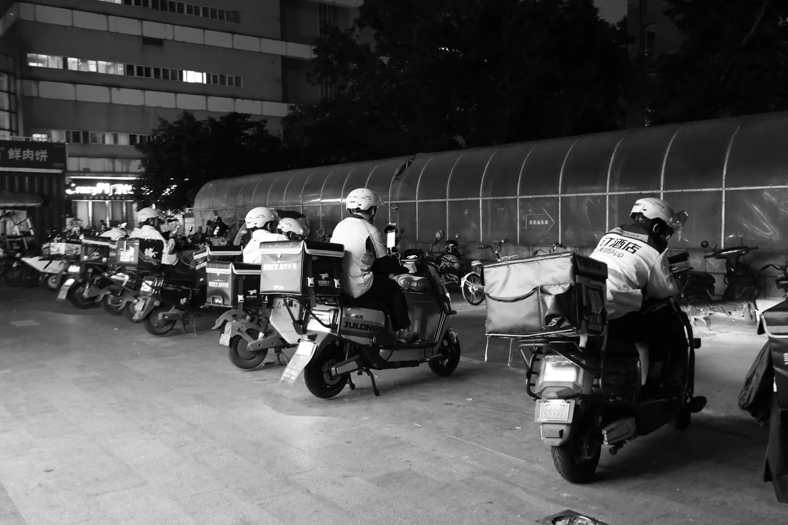 Food delivery drivers on scooters gather at night for dispatch in an urban setting. Stock photo illustrating Greaves Cotton's fund raise story.