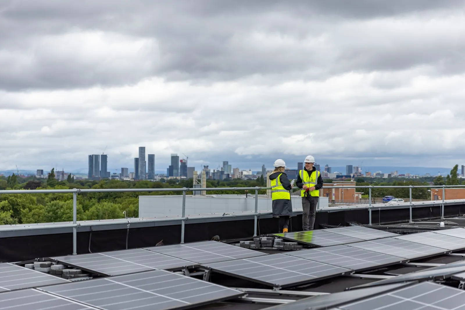 Two workers checking solar panels on a rooftop with a city skyline in the background. Stock photo illustrating Pritika Auto Industries' expansion story.