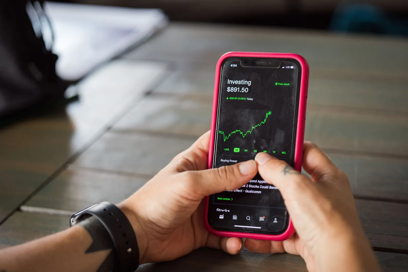 A person holding a smartphone with a stock market app displaying analytics and stock prices. Stock photo for the ALFA News guide: SMS vs App Stock Alerts: Comparing Speed and Reliability.