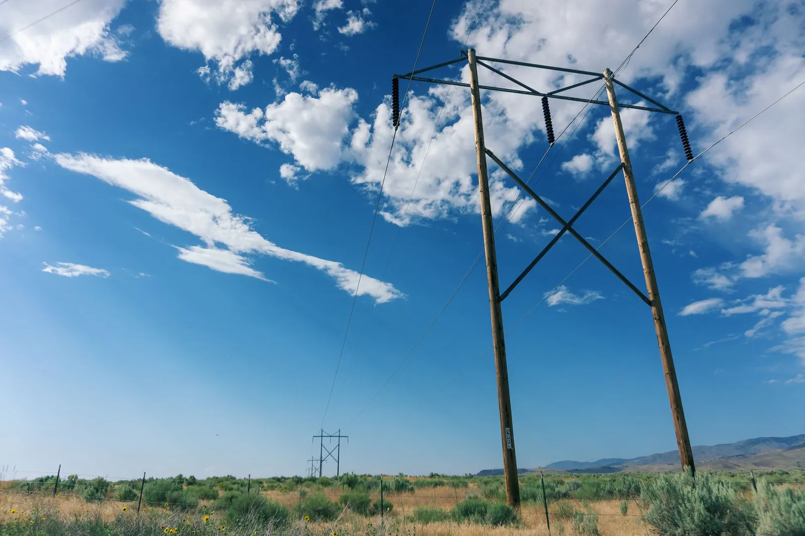 Scenic view of high voltage power lines in a field with a bright blue sky and fluffy clouds. Stock photo illustrating HEC Infra Projects' new order story.