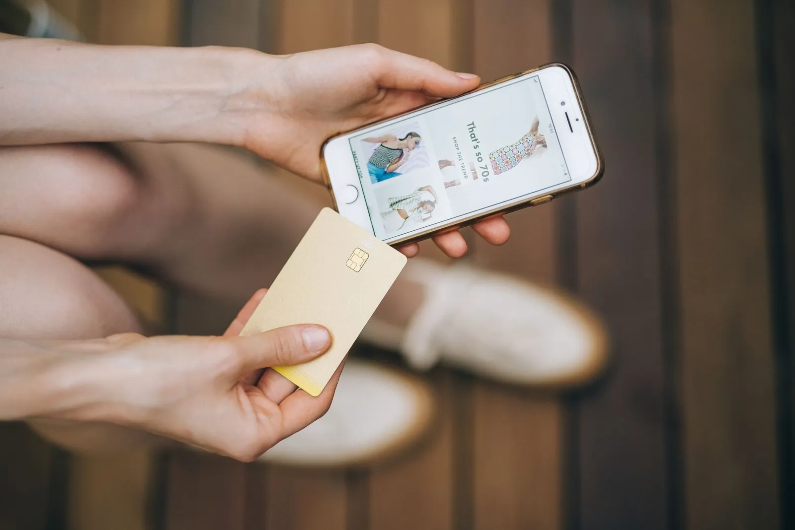 Hands holding smartphone and credit card for online shopping on a wooden floor. Stock photo illustrating SBI Cards and Payment Services' product launched story.
