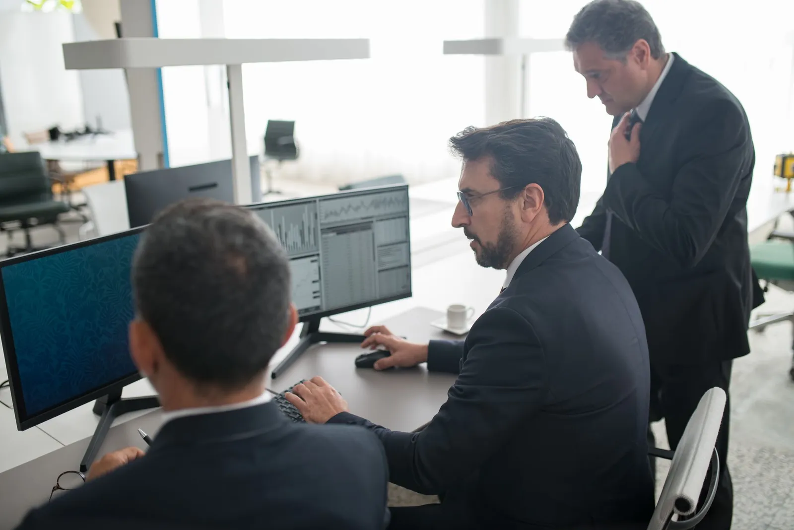 Colleagues in a modern office reviewing stock market trends and data on multiple screens. Stock photo illustrating Kanel Industries' fund raise story.