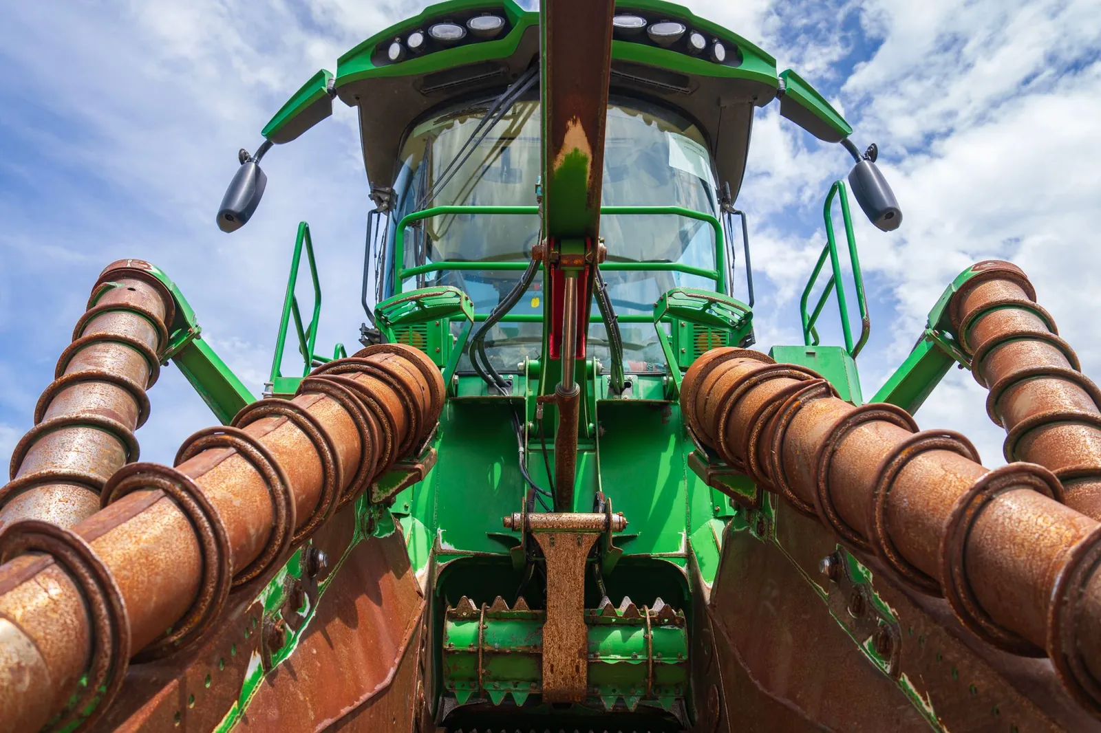 Detailed view of a green agricultural harvester against a blue sky, highlighting its machinery components. Stock photo illustrating Uniparts India's earning call story.