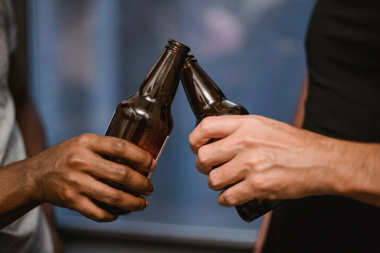 Close-up shot of two individuals clinking beer bottles in a casual indoor setting. Stock photo illustrating Som Distilleries & Breweries' fund raise story.
