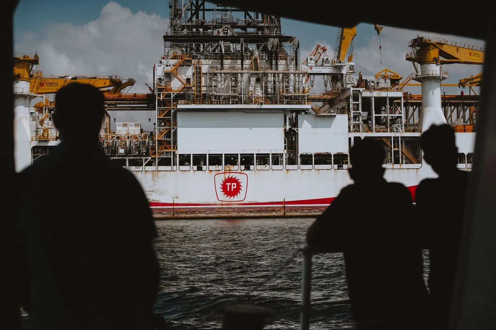 Silhouetted figures observing a large offshore oil rig at sea, emphasizing maritime industry. Stock photo illustrating Seamec's new order story.