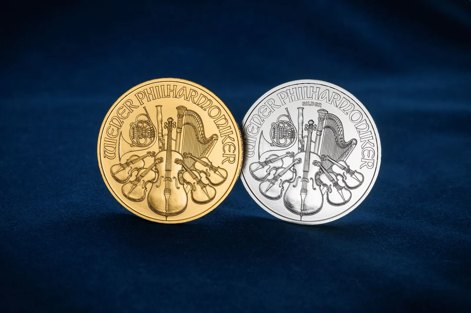 Close-up of gold and silver Wiener Philharmoniker coins displayed on blue velvet cloth. Stock photo illustrating Grover Jewells' partnership story.