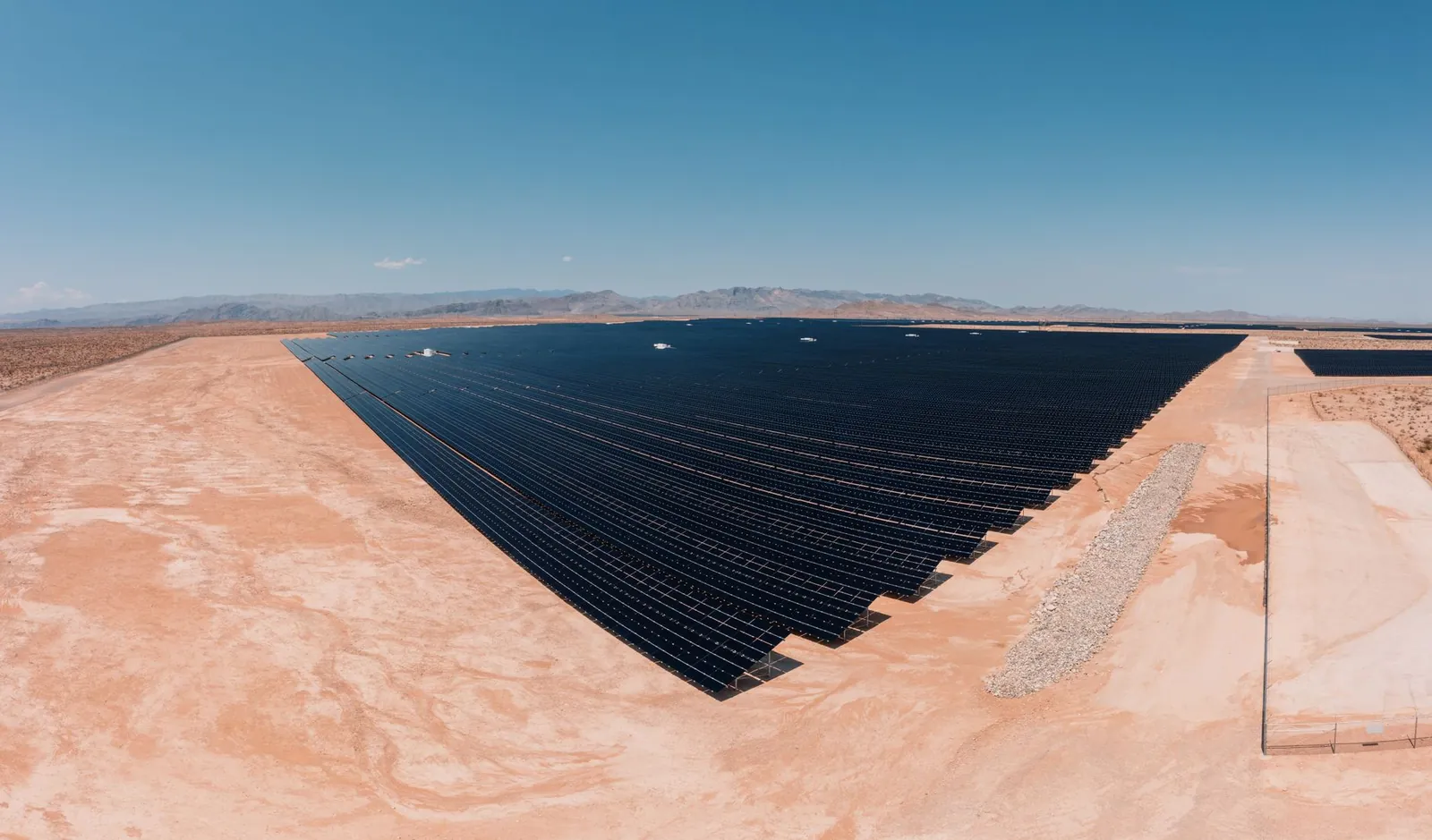 Aerial view of a large solar farm in a desert setting under a clear blue sky. Stock photo illustrating Sterling and Wilson Renewable Energy's new order story.