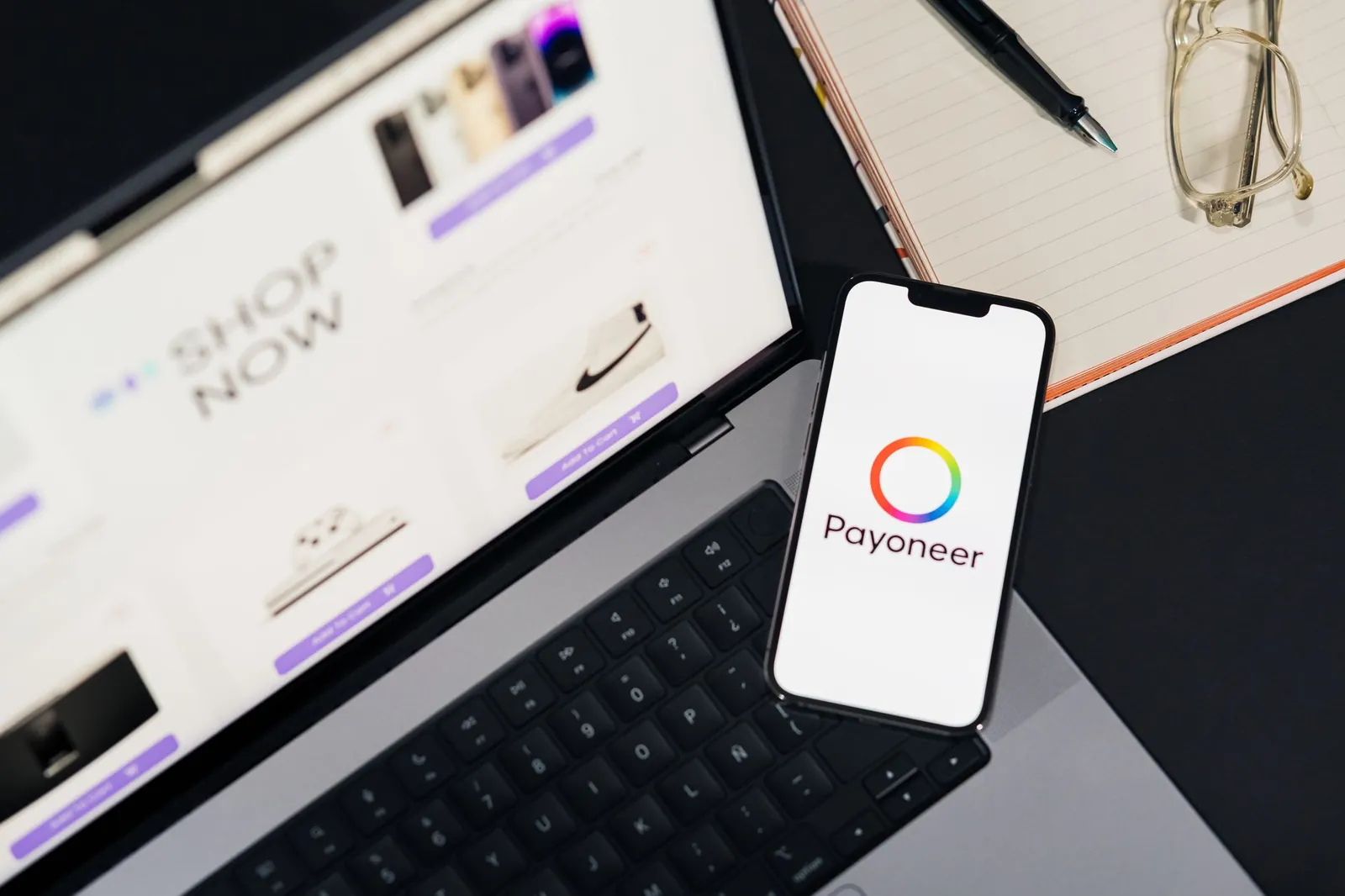 Mobile phone with Payoneer app on screen next to laptop displaying online shopping site. Stock photo illustrating Akiko Global Services' earning call story.