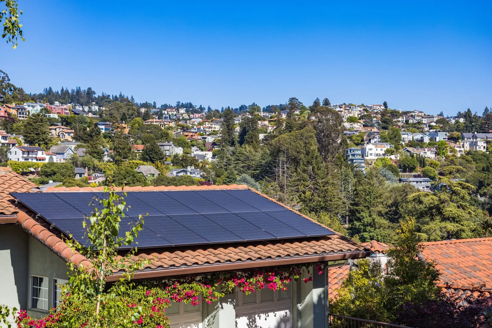 Solar panels on a suburban home, surrounded by lush greenery and a sunny blue sky. Stock photo illustrating Smarten Power Systems' product launched story.