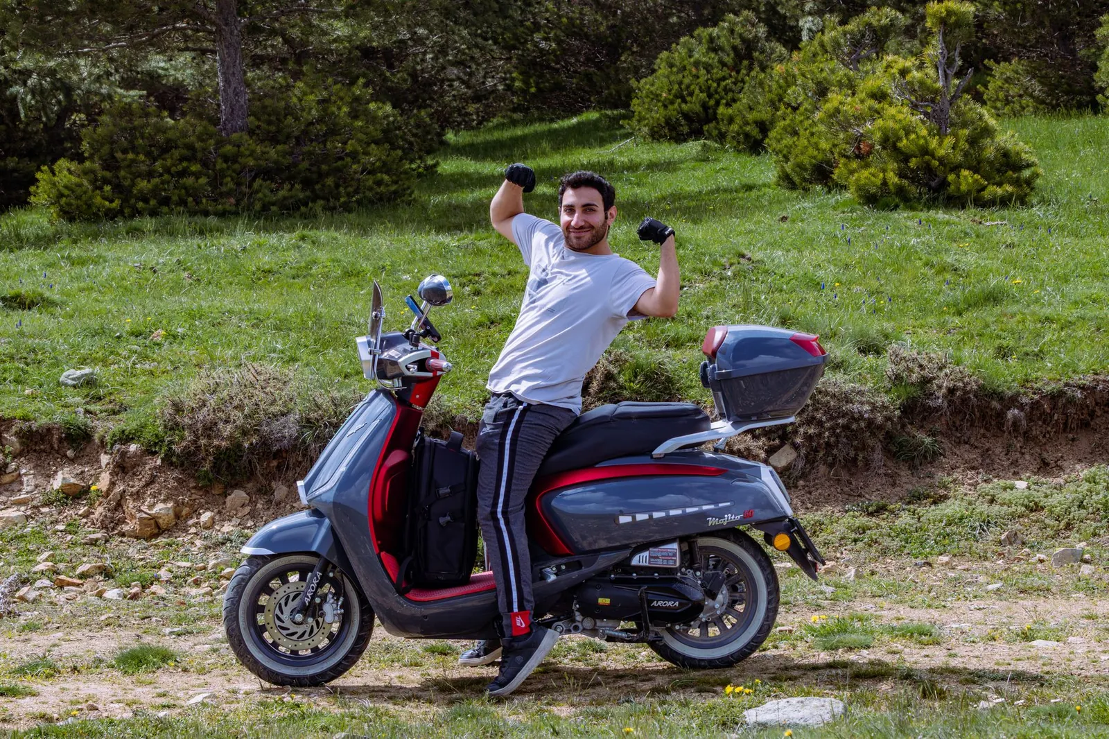 Man flexing on a scooter surrounded by lush greenery in a natural setting. Stock photo illustrating TVS Motor Company's product launched story.