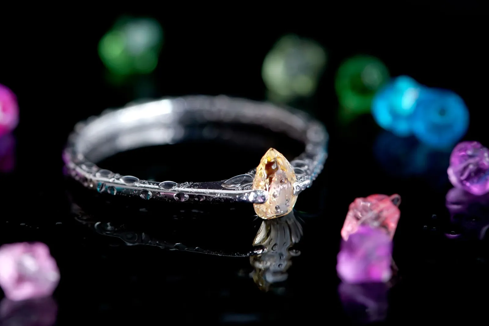A stunning diamond ring set against colorful gemstones on a reflective surface. Stock photo illustrating Mini Diamonds (India)'s product launched story.
