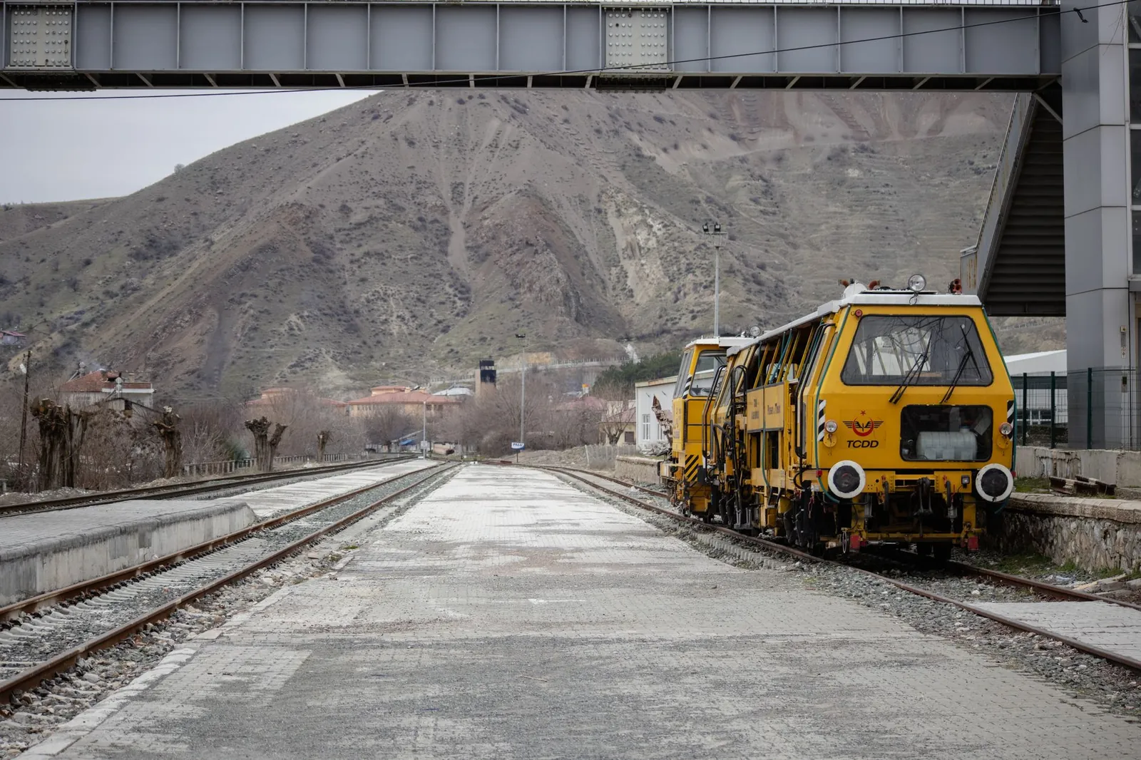 Yellow tamping machines on railway tracks in Palu, Elazığ, with scenic mountains in the backdrop. Stock photo illustrating Afcons Infrastructure's new order story.