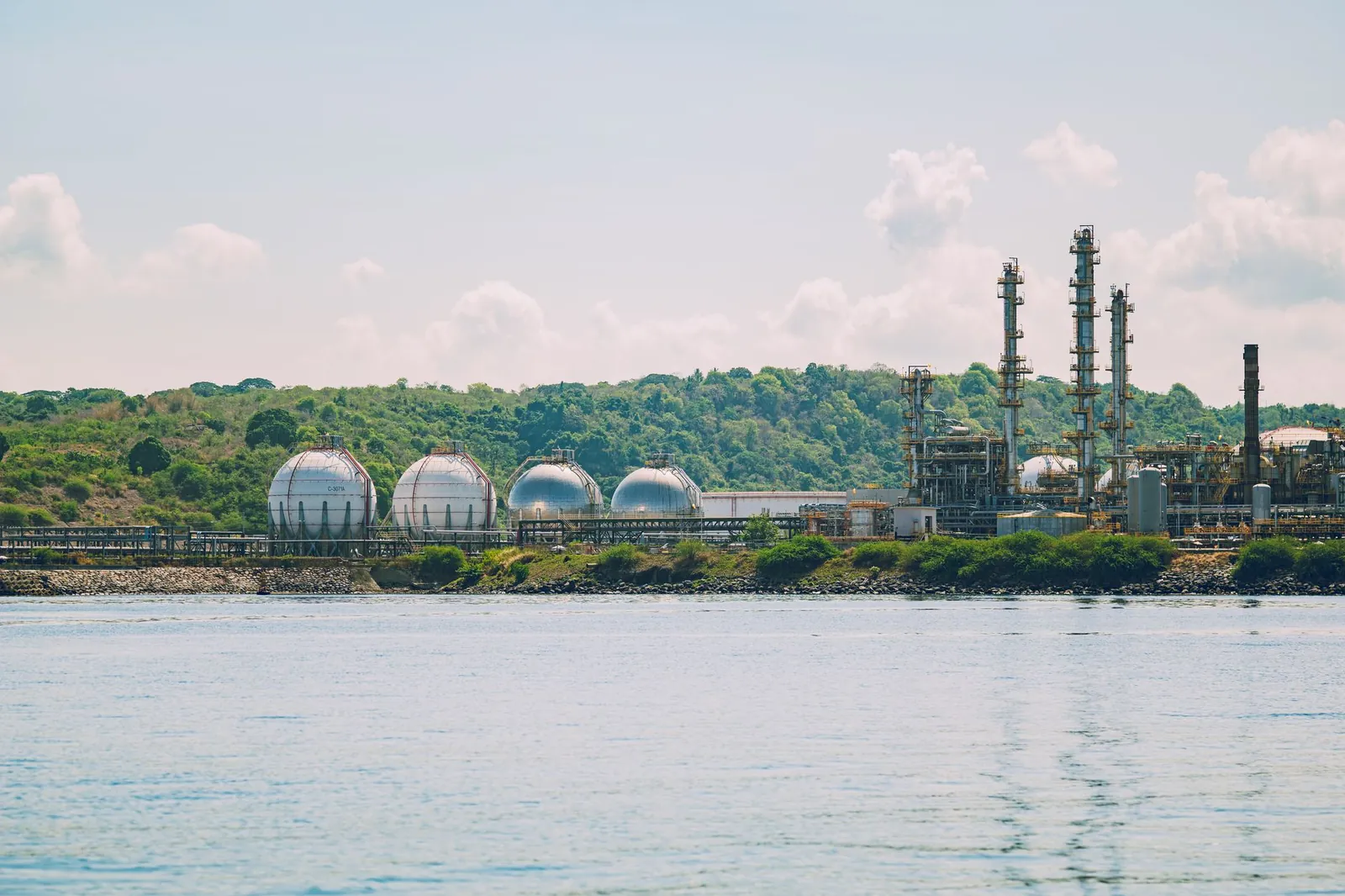 A scenic view of a coastal industrial gas storage facility with spherical tanks and tall chimneys. Stock photo illustrating Neogen Chemicals' earning call story.