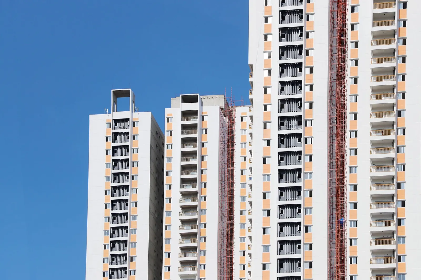 Tall residential skyscrapers under construction with scaffolding against bright blue sky. Stock photo illustrating Sumit Woods' new order story.