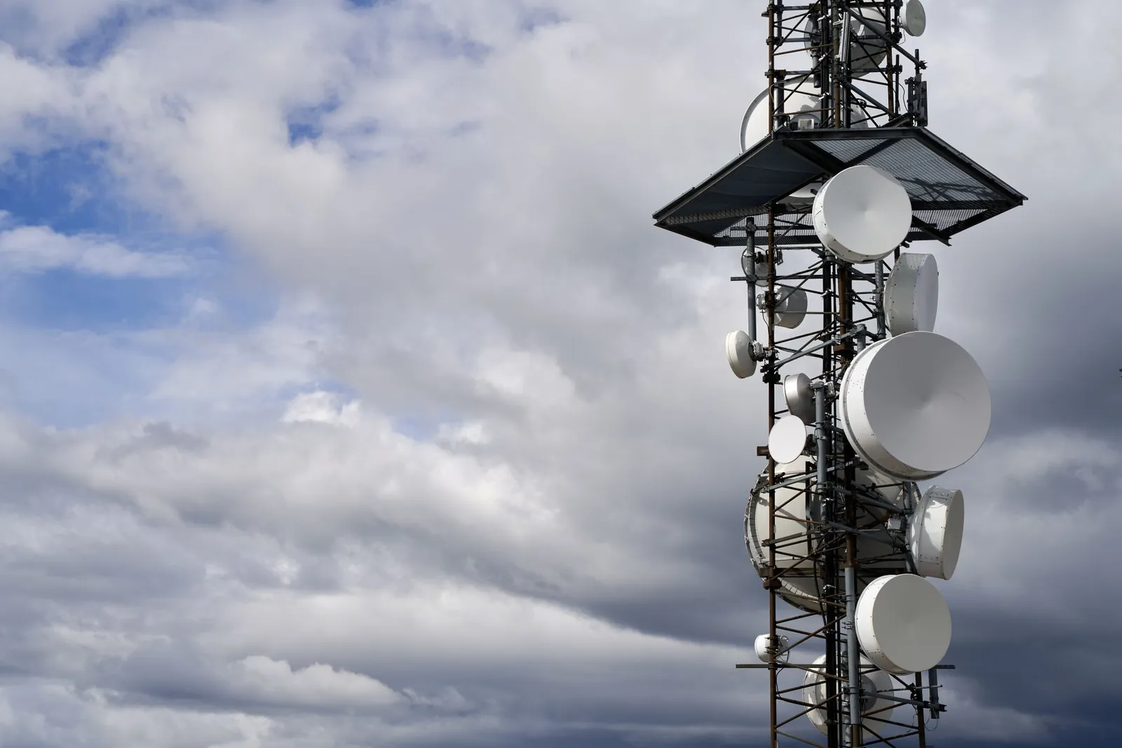 A telecommunication tower equipped with satellite dishes against a cloudy sky. Stock photo illustrating Subex's new order story.