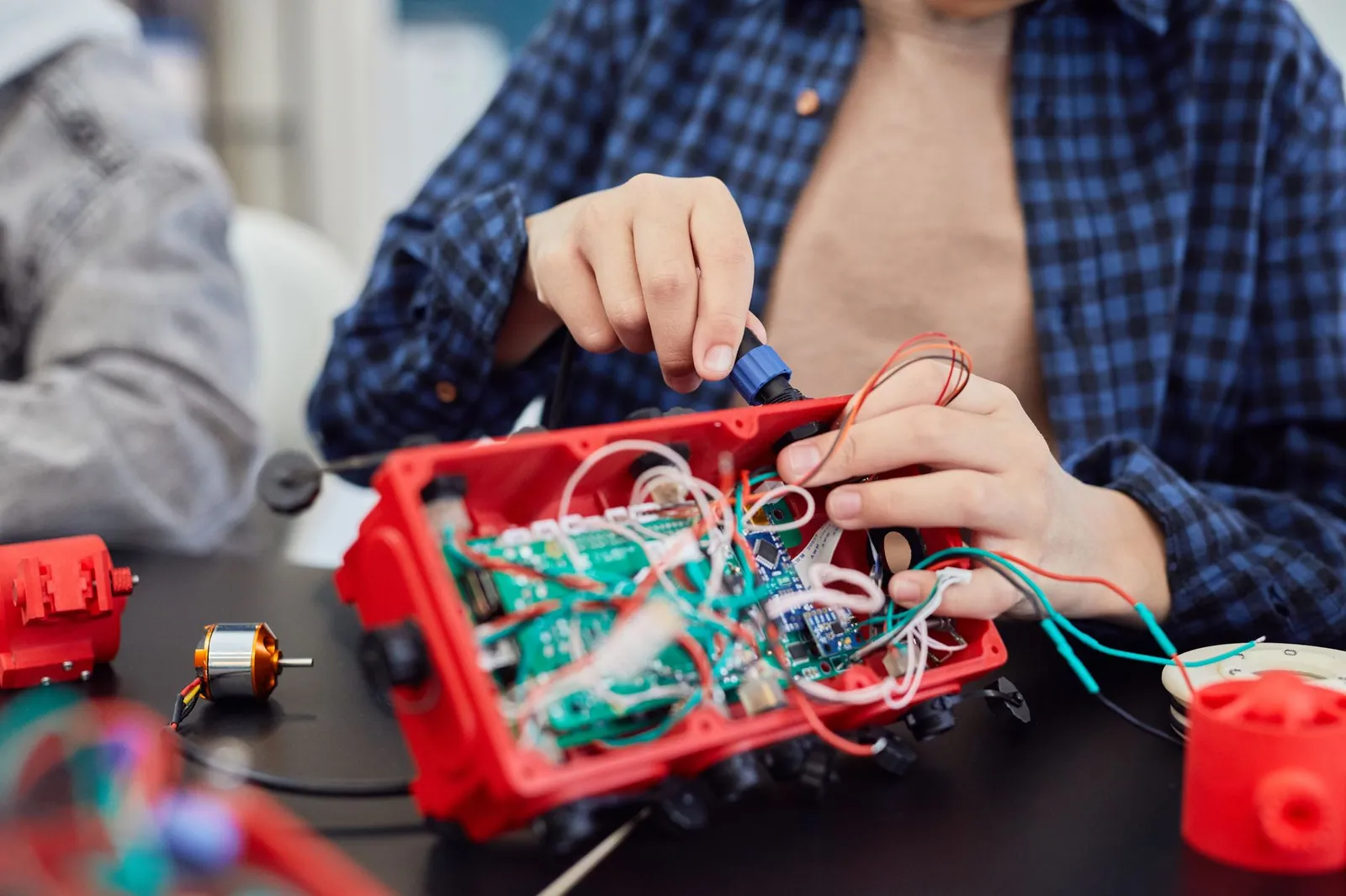 Close-up of hands assembling a robotic project with wires and circuits. Stock photo illustrating Apollo Micro Systems' financial results story.