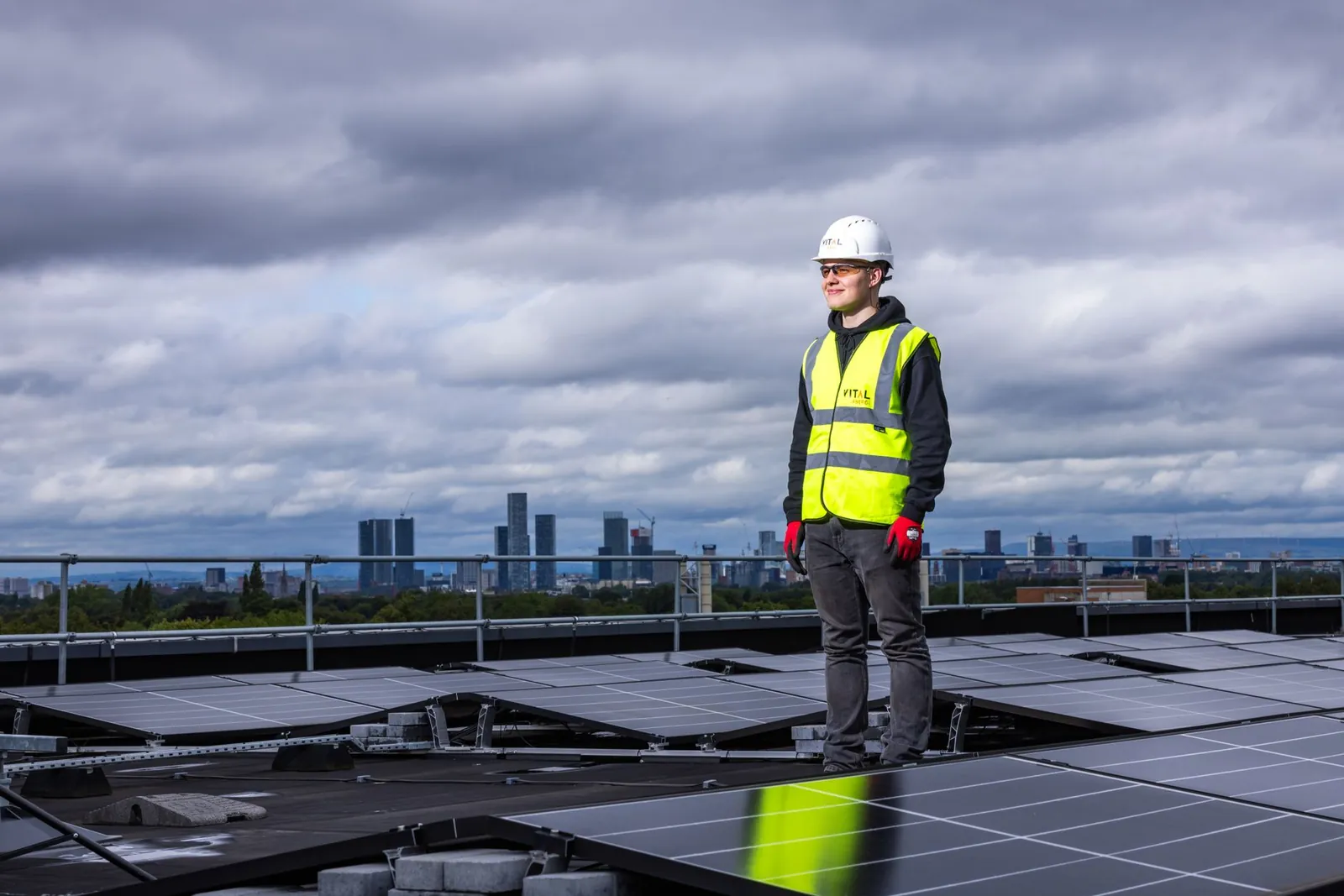Engineer standing on rooftop inspecting solar panels with city skyline in background. Stock photo illustrating Insolation Energy's new order story.