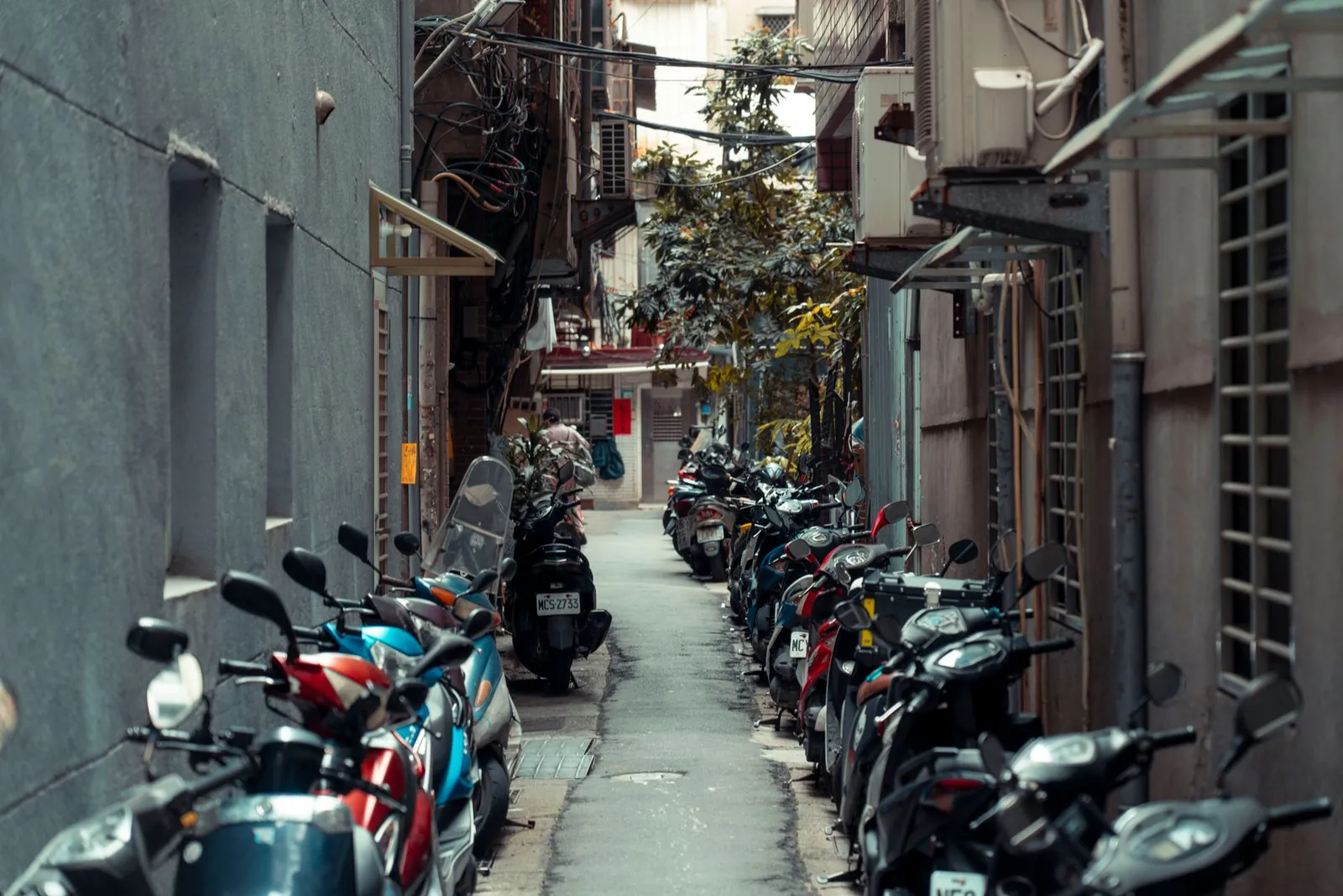 A narrow urban alleyway lined with parked scooters on both sides, creating a bustling city atmosphere. Stock photo illustrating TVS Motor Company's product launched story.