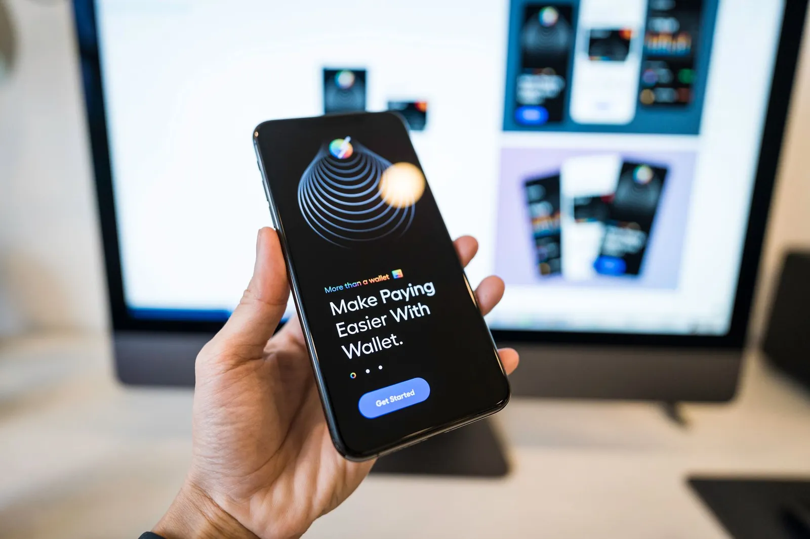 Hand holding smartphone displaying digital wallet app interface, blurred monitor in background. Stock photo illustrating Gyftr's partnership story.