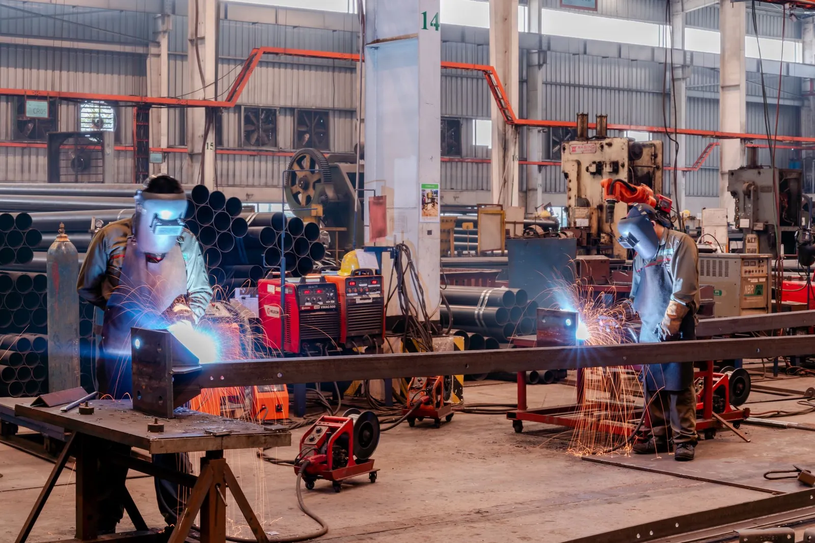 Two welders wearing protective gear working in a busy industrial factory workshop. Stock photo illustrating DEE Development Engineers' new order story.