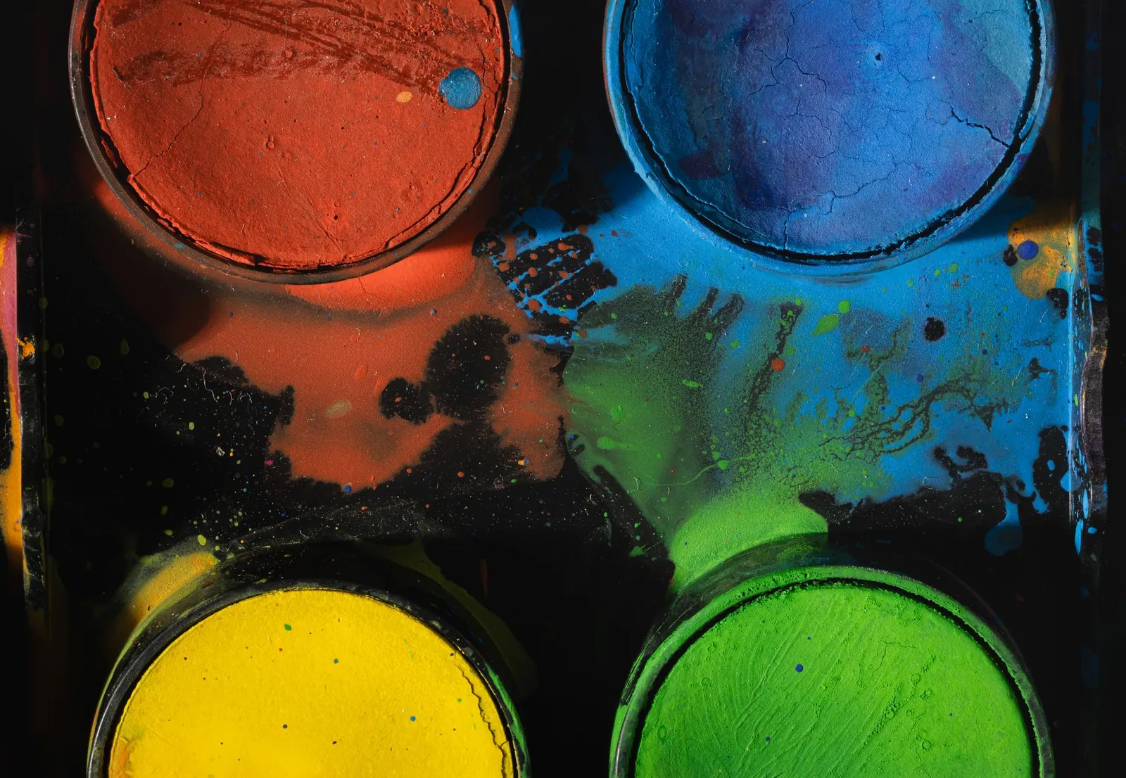 A close-up of a colorful paint palette showing vibrant pigments in red, blue, yellow, and green. Stock photo illustrating Poddar Pigments' partnership story.
