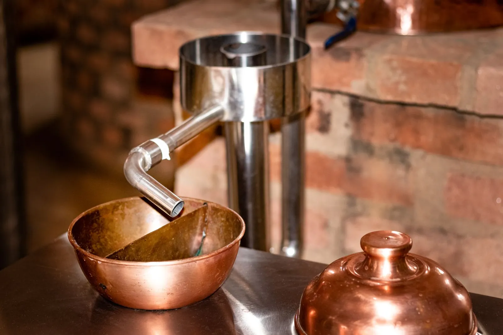 Close-up of copper distillation apparatus against a rustic brick background, indoors. Stock photo illustrating Adani Enterprises' financial results story.