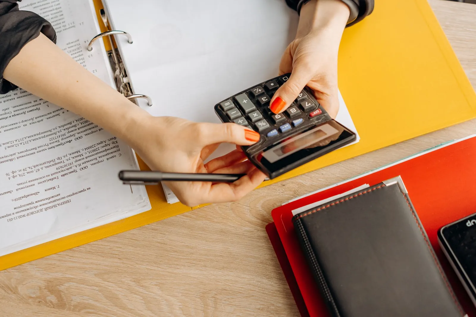 Hands using a calculator at a desk with documents and folders, ideal for finance or accounting themes. Stock photo for the ALFA News guide: Debt-to-Equity Ratio: A Guide for Indian Investors.