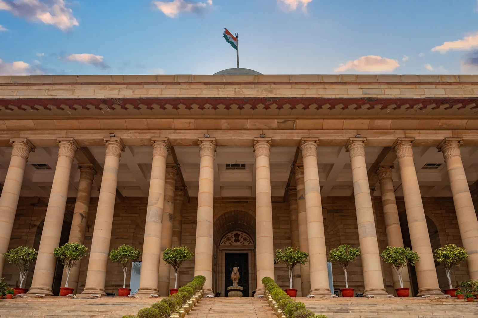 Government building in New Delhi featuring columns and an Indian flag under a vibrant sky. Stock photo illustrating Choice International's new order story.
