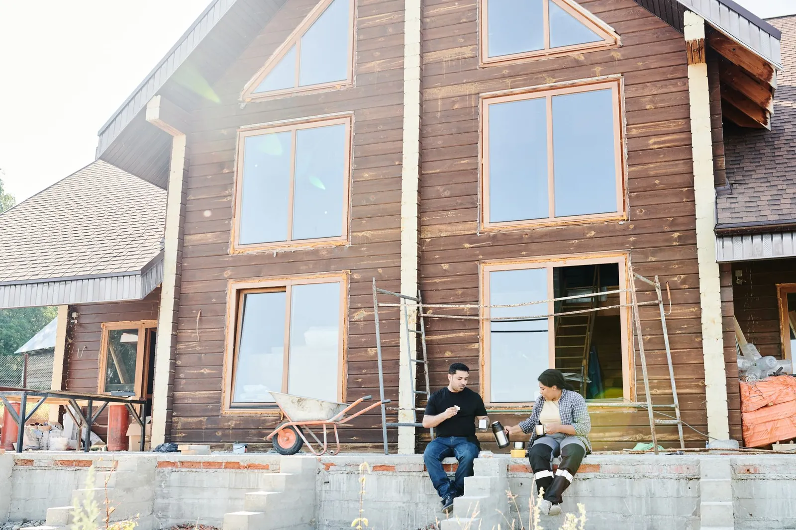 Two individuals enjoying coffee during a break at a wooden house construction site. Stock photo illustrating Atal Realtech's new order story.