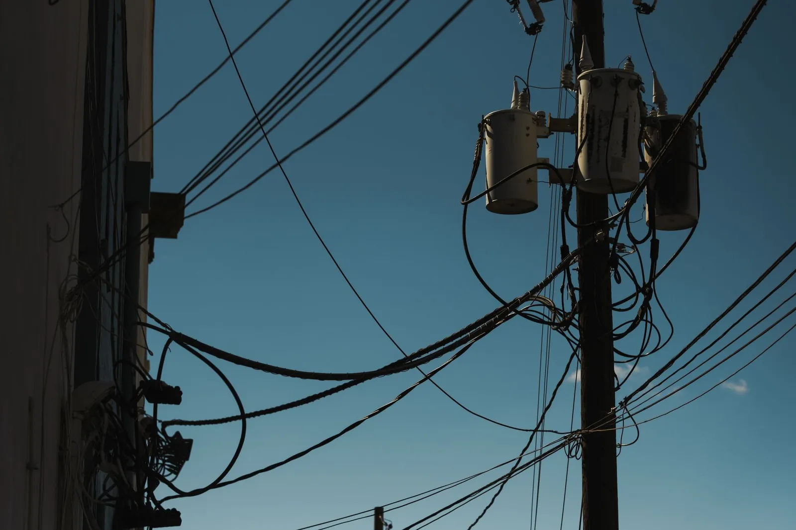 Low angle view of power lines and transformers against a clear blue sky, depicting modern electricity infrastructure. Stock photo illustrating Kanohar Electricals' new order story.