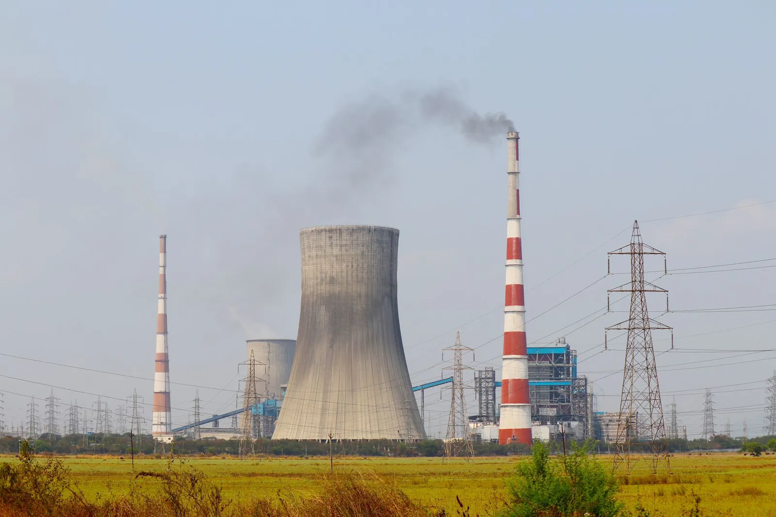 Aerial view of an industrial power plant in Vijayawada, India, with cooling towers and chimneys emitting smoke. Stock photo illustrating SJVN's production started story.