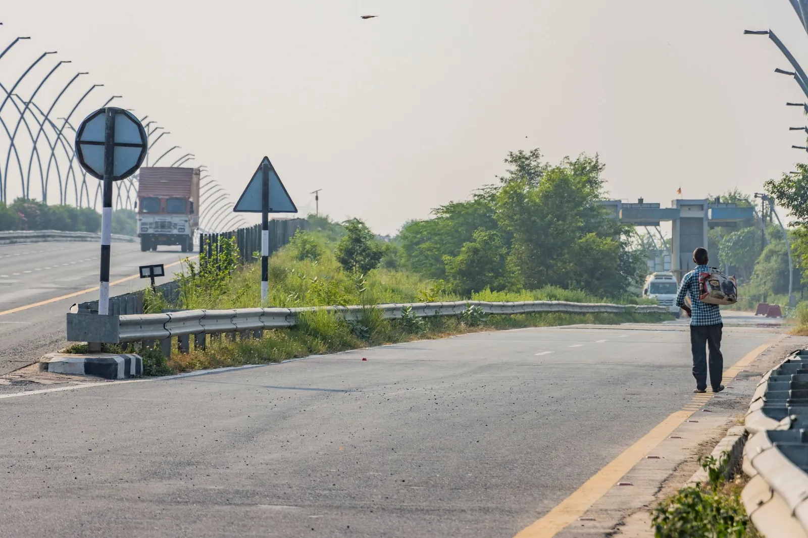 A man walks along the highway in Deeg, Uttar Pradesh, India, with vehicles in the distance. Stock photo illustrating B.R.Goyal Infrastructure's new order story.