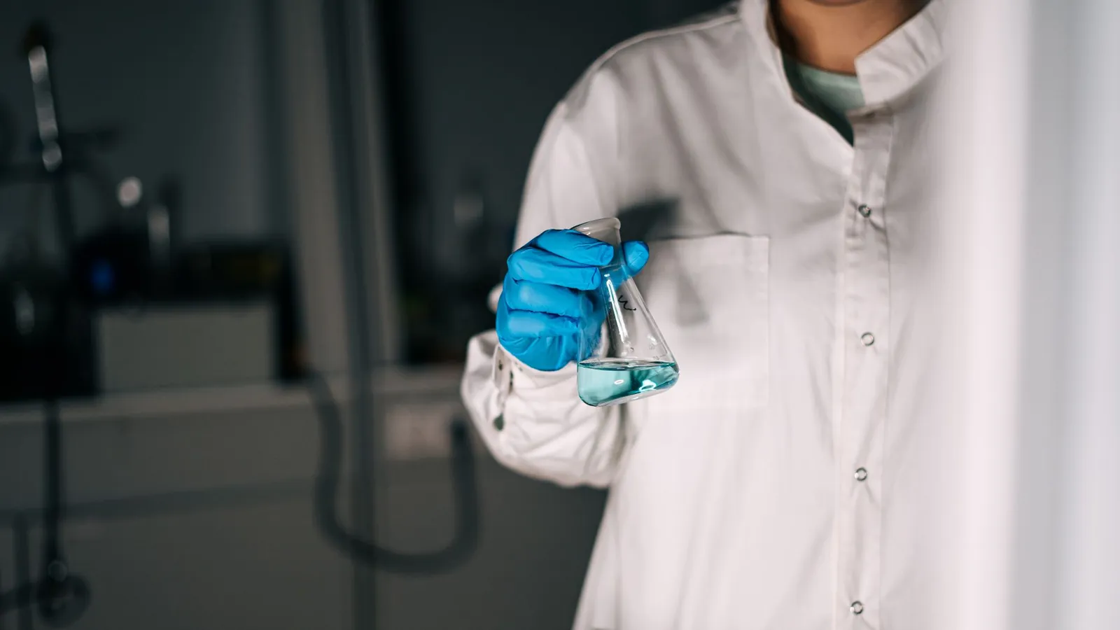 Scientist in white coat holding a flask with blue liquid in a laboratory, showcasing scientific research. Stock photo illustrating Navin Fluorine International's financial results story.